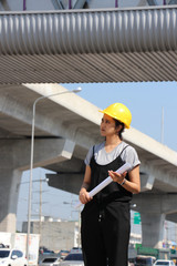 Female civil engineer or architect with yellow helmet, standing with project drafts while in hand.