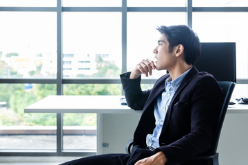 Young Asian businessman Sitting in a modern office is thinking and analyzing to find solutions to improve business performance