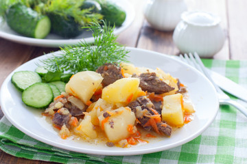 Stewed potatoes with chicken liver and carrots on a white plate, selective focus
