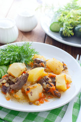 Stewed potatoes with chicken liver and carrots on a white plate, selective focus