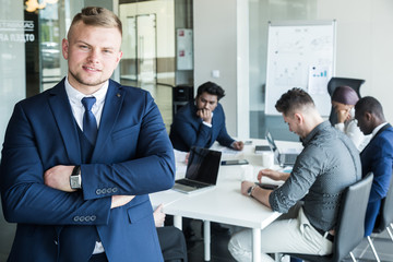 Business man stands on the background of partners. A team of young businessmen working and communicating together in an office. Corporate businessteam and manager in a meeting.