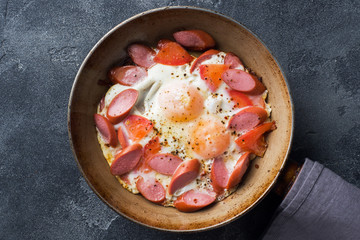 Pan with fried eggs sausages and tomatoes on the table. Rich homemade Breakfast.