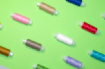 needlework, craft, sewing and tailoring concept - row of colorful thread spools on green background, flat lay, top view, blured background