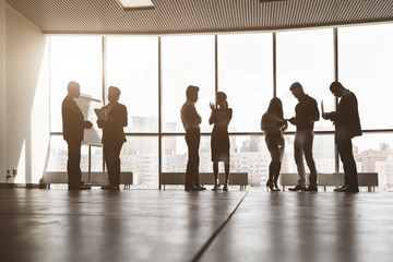 Silhouettes of people against the window. A team of young businessmen working and communicating together in an office. Corporate businessteam and manager in a meeting.