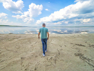 Man is walking close up on the amazing background of the sea and reflection of the sky in water