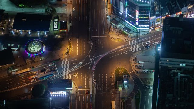 Timelapse zoom out Osaka downtown district street highway crossroad with changing traffic lights and cars flow with crosswalks among highrise buildings at evening rush hour under night illumination