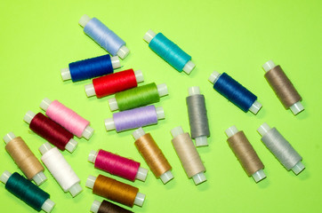 needlework, craft, sewing and tailoring concept - row of colorful thread spools on green background, flat lay, top view