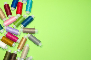 needlework, craft, sewing and tailoring concept - row of colorful thread spools on green background, flat lay, top view