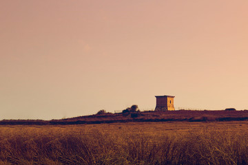 Fototapeta premium Outdoor architecture of an ancient Venetian tower in Cyprus, Pervolia, neughborhood of Larnaca. Sunset. Brown duotone. Horizontal with copy space