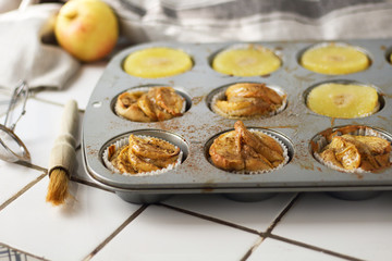 Muffins cupcakes with pineapple circles and apple slices in a cupcake muffin tray, on kitchen white tile near with pastry brush. Cake dessert photo for cook book recipe top view
