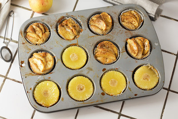 Muffins cupcakes with pineapple circles and apple slices in a cupcake muffin tray, on kitchen white tile near with pastry brush. Cake dessert photo for cook book recipe top view