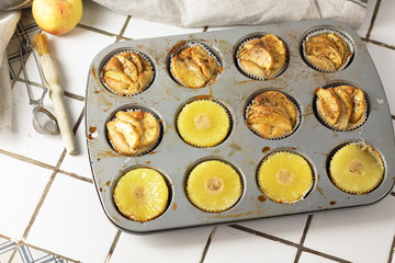 Muffins cupcakes with pineapple circles and apple slices in a cupcake muffin tray, on kitchen white tile near with pastry brush. Cake dessert photo for cook book recipe top view