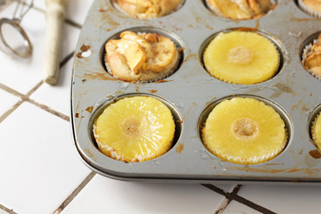 Muffins cupcakes with pineapple circles and apple slices in a cupcake muffin tray, on kitchen white tile near with pastry brush. Cake dessert photo for cook book recipe top view