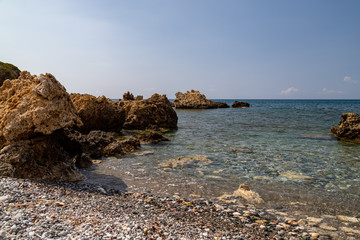 Fototapeta na wymiar View at the rocky coastline of Plimmiri on Rhodes island, Greece with gravel beach and rocks in the water
