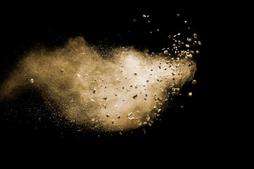 Split debris of brown stone exploding with brown powder against black background.