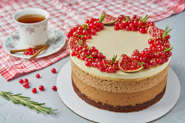 Round homemade cake decorated with red currants, figs, cinnamon and rosemary with tablecloth, Cup and saucer on a light background concrete table.