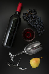 Bottle of red wine, glass, corkscrew  and ripe grapes