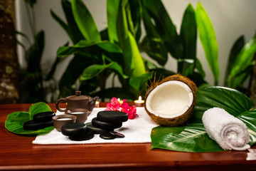 A terry towel with a clay teapot and cups for drinks with milk, stones for stone therapy, candles, a mangolia flower and a twisted terry towel