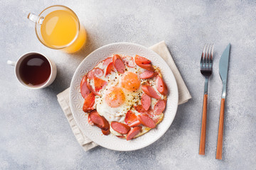 Fried eggs sausages and tomatoes on a plate on the table. Rich homemade Breakfast. Gray concrete background. Copy space.