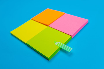 Four small sets of yellow, orange, pink, green stickers folded in a square on a blue background, one of which has a green sticker in the form of a strip. Close-up. Place for notes.