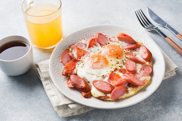Fried eggs sausages and tomatoes on a plate on the table. Rich homemade Breakfast. Gray concrete background. Copy space.