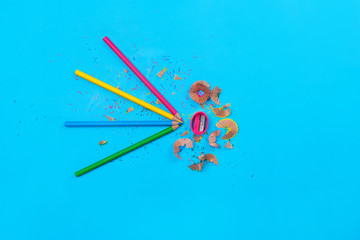 Colored pencils folded together with shavings from pencils in the center on a blue background....