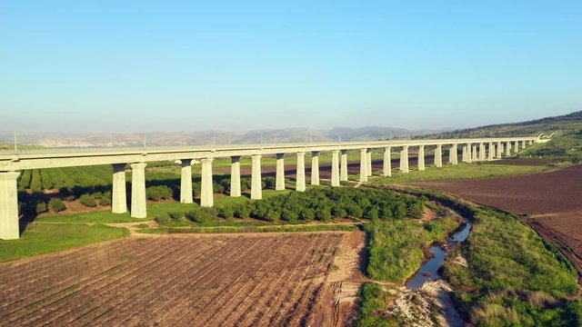 Aerial: Lush Fields and Farmland Cut Across by Tall Rail Overpass on Sunny Day Near Modiin
