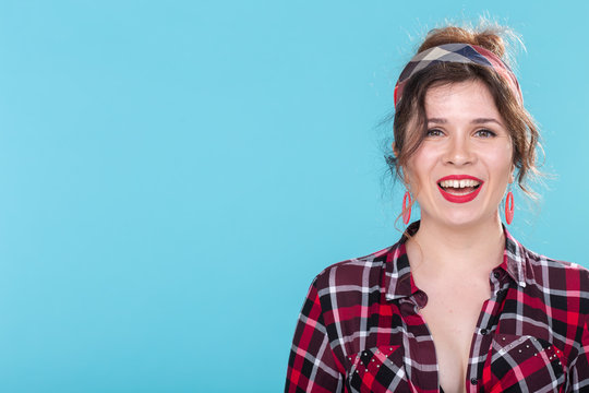 Positive beautiful young woman in a plaid vintage shirt looking at the camera and smiling posing on a blue background with copyspace