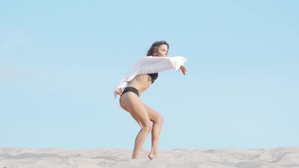 Full length shot of a gorgeous seductive woman dancing in black bikini. Stunning flexible female dancer performing in the desert on sand. Femininity, sensuality concept