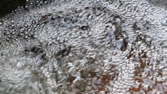Sprudelnder flie&szlig;endes Strudel Wasser am Bachlauf mit Wellen, Wassertropfen und Luftblasen.	