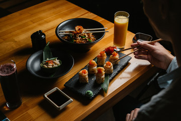 young man eating sushi rolls and wok in a restaurant