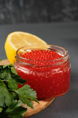 black and red caviar in glass jars with parsley and lemon on a gray background. Russian national cuisine