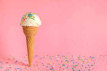vanilla flavor ice cream in waffle cone with strewed multicolor sprinkles on pink background