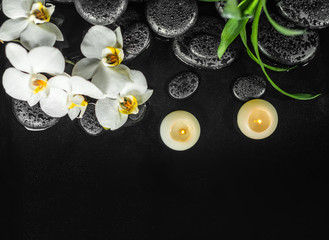 top down of spa composition white orchid (phalaenopsis), candles and black zen stones with drops in water