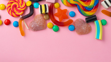 candies and jelly colorful array of different childs sweets and treats over pink background with copy space, panorama