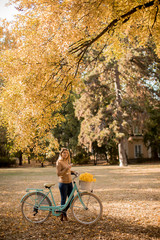 Young woman with bicycle using smartphone in autumn park