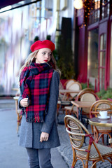 young girl in a red beret and a gray coat near a cafe © Alina