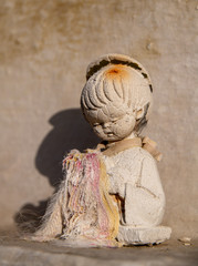 Verwitterte Puppe vor einer Grabplatte in Spanien