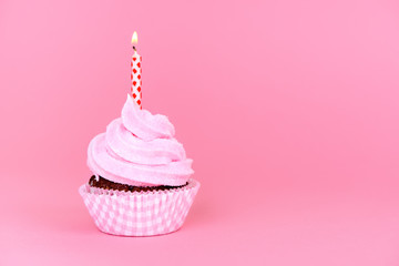 birthday cupcake decorated whipped cream icing and candle on pink background, concept of baby party