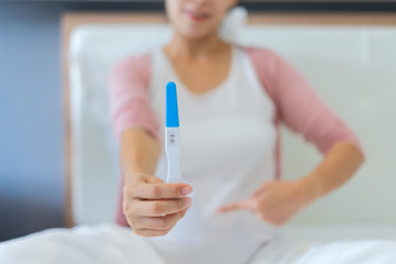 Close up of woman hand holding a positive home pregnancy test in bedroom at home