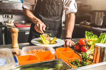 Professional chef cooking in the kitchen restaurant at the hotel, preparing dinner. A cook in an apron makes a salad of vegetables and pizza.