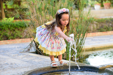 smiling little girl playing with water from a fountain
