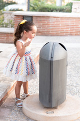 Little girl taking garbage in to the bin in the park