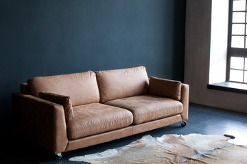 Luxurious living room interior. Brown leather sofa in a dark room by the window. Carpet made of genuine leather. Grunge interior. Office interior business. Loft Room. classic interior. Antique sofa