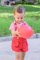 little boy with red pants and white shirt playing with a red balloon in the park