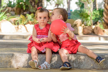 twin brother giving his sister a kiss on the cheek. Children playing in the park with a red balloon.