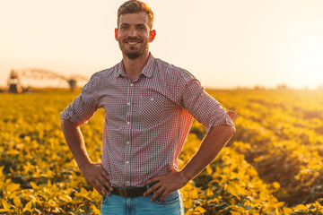 Naklejka na ściany i meble Portrait of farmer standing in soybean field at sunset.