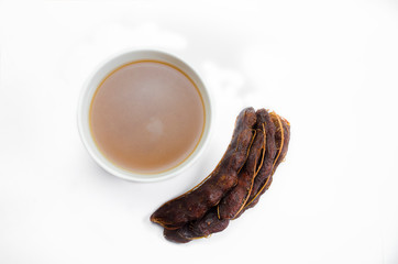 Fresh tamarind fruits brown and juice in a white cup on top view isolated on white background