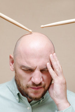 Portrait of a man with his eyes closed and drumsticks over his head. Image of severe headache, migraine, stress, noise.