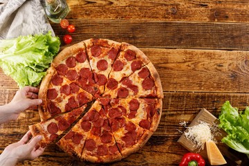 Pepperoni pizza on a wooden table. Still life with hands and ingredients. Copy space.